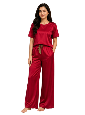 Woman wearing a red pajama set standing in a minimalistic room with a plant and framed picture.
